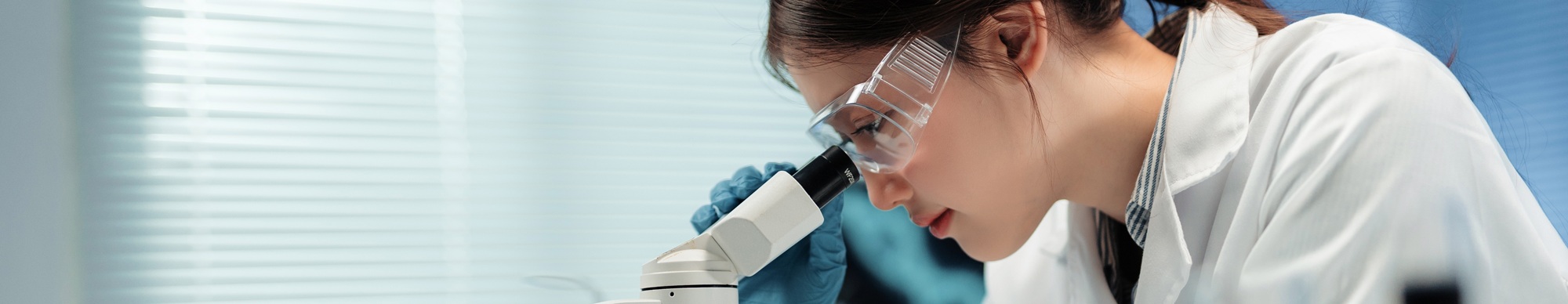 Young,Female,Scientist,Looking,Through,A,Microscope,In,A,Laboratory,